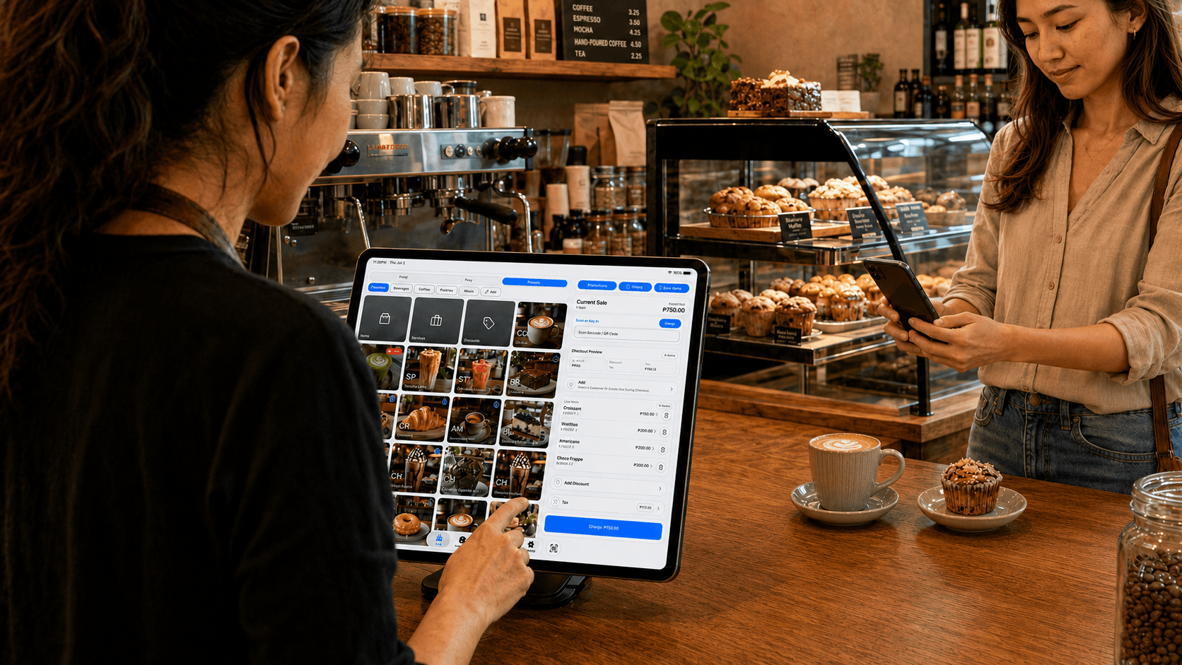 Cafe counter staff using the BizAssist POS tablet with product tiles and a current sale review visible.